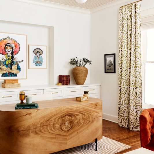 Green abstract custom curtain hanging on a rod in front of a window in an office with a wooden desk and rust colored couch