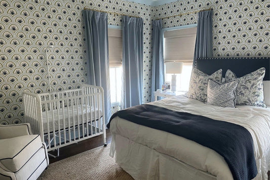 Bedroom with a white bed with two Green Tiger Custom pillows and a Blue and White Custom pillow on top next to two illuminated windows styled with Sky Blue Velvet Curtains and Art Deco Palm Pattern Custom Wallpaper behind a white crib 