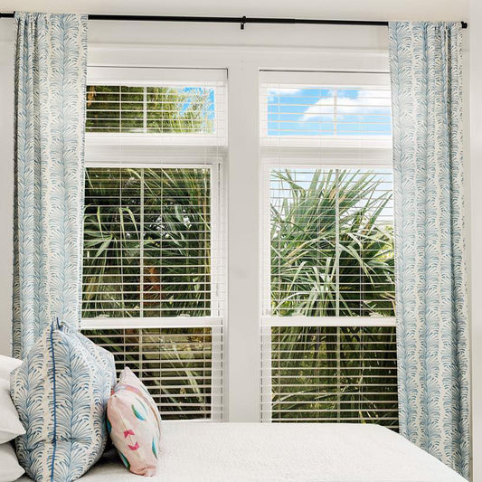 Window close-up styled with Sky Blue Botanical Stripe Custom Curtains in front of a white bed with a Sky Blue Botanical Stripe Custom Pillow and palm trees outside the window