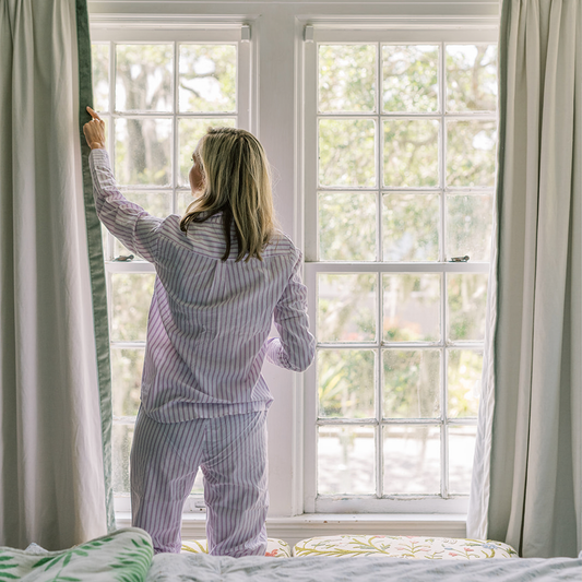 Close up of a hand taping a natural white curtain panel's pleats together in front of a window