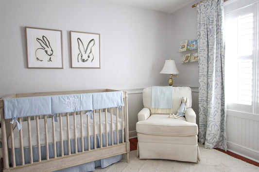 Nursery room with with a cream armchair with a crib on one side and an illuminated window in the other styled with Sky Blue Custom Curtains 