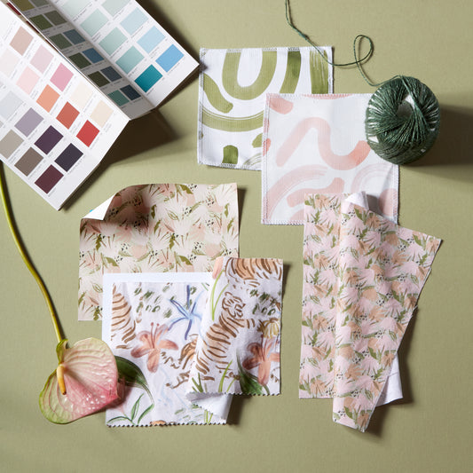 Interior design moodboard with paint chips, abstract pink and green fabric swatches, pink floral fabric swatch and pink chinoiserie tiger fabric swatch with a green background 