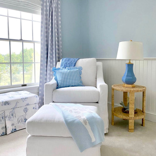 Nursery room with white sofa chair with blue gingham printed pillow next to a window styled with Sky Blue Pattern Custom Curtains 