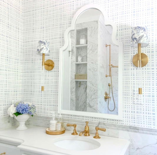 Bathoom with blue gingham wallpaper styled with a white mirror and brass light fixtures and faucet on a white vanity