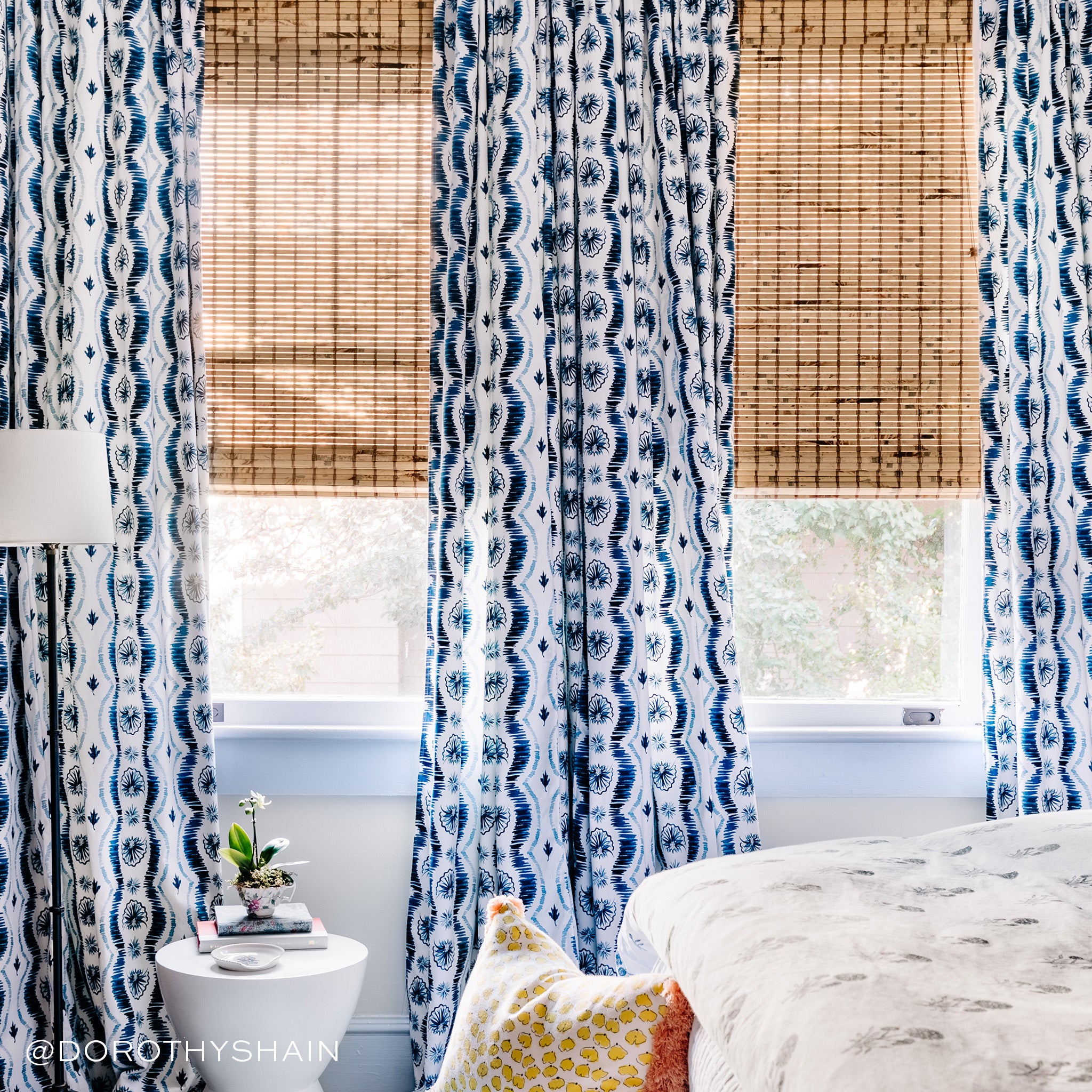 Blue Ikat printed curtains by bed and white coffee table with two books and flower on top