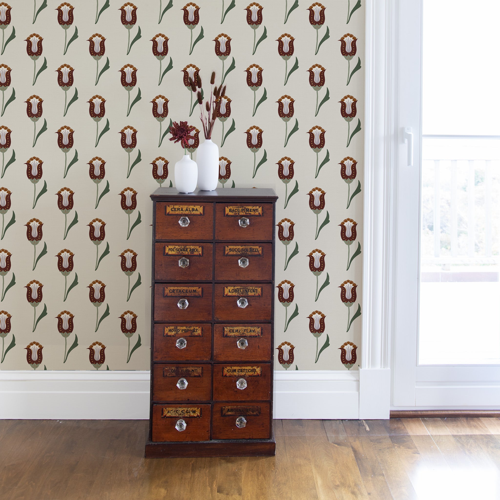 abstract floral maroon and forest green wallpaper on a wall with a brown cabinet in front with vases with flowers on top