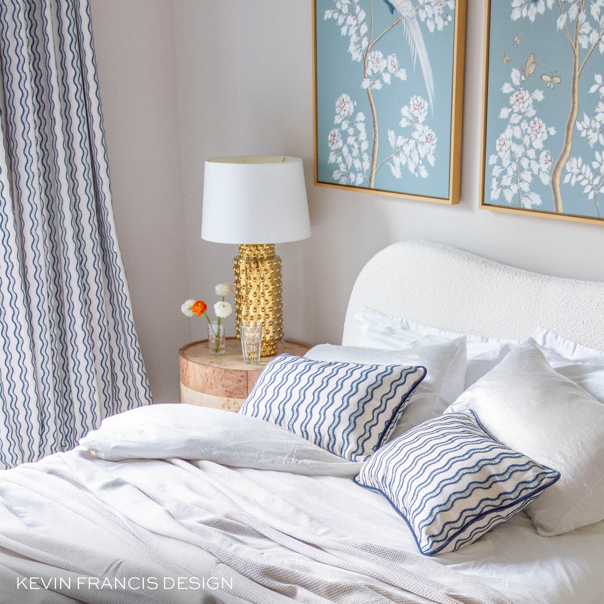 embroidered cream with navy wavy blue lines curtains and pillows in a bed room with blue and white floral artwork on the walls