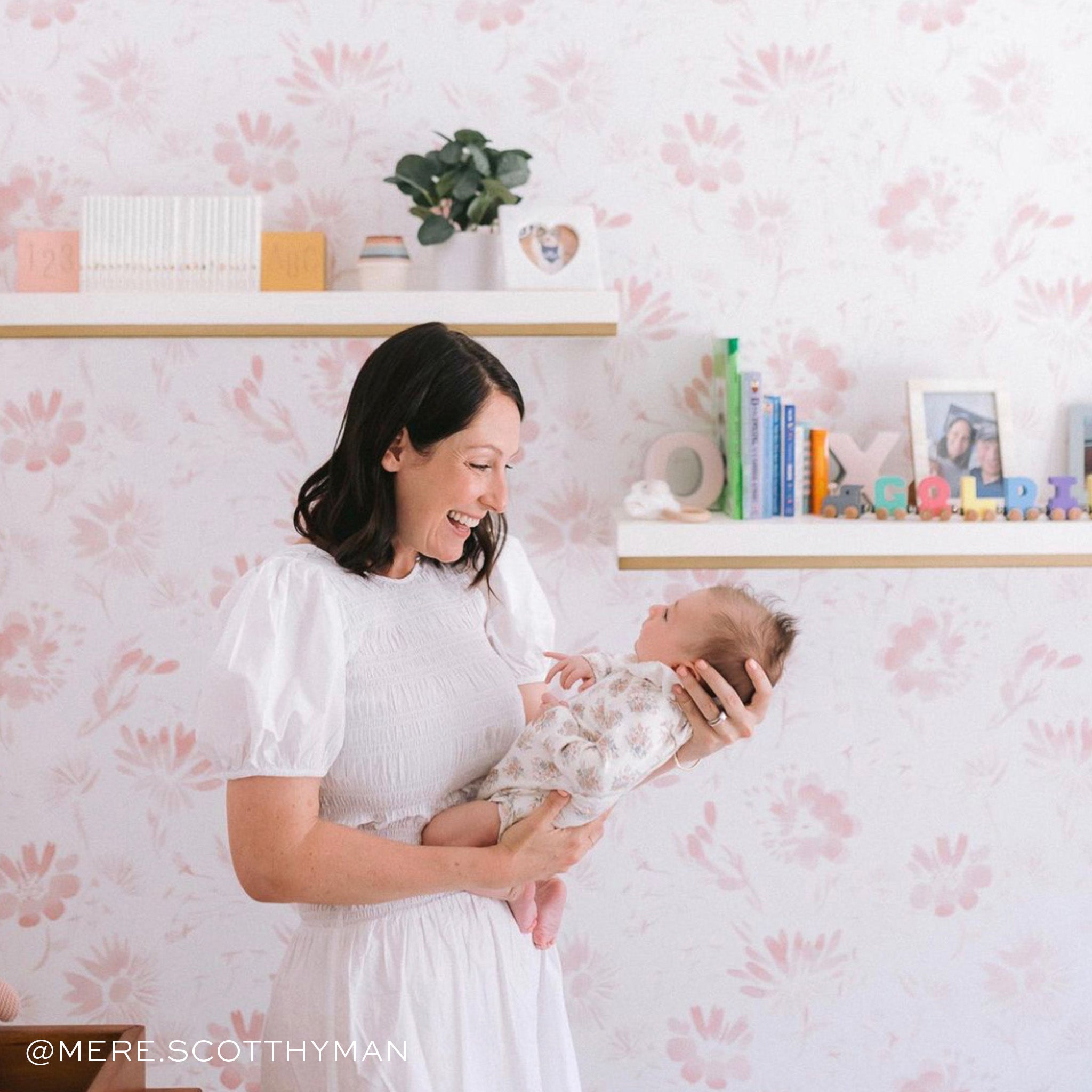Pink Floral Wallpaper on nursery room with two shelves and mother holding her baby while smiling