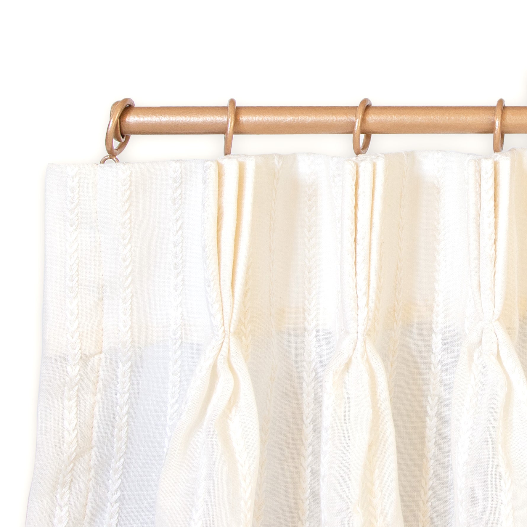 close up picture of pinch pleat white curtains with embroidered white stripes on it hung on a light brown rod