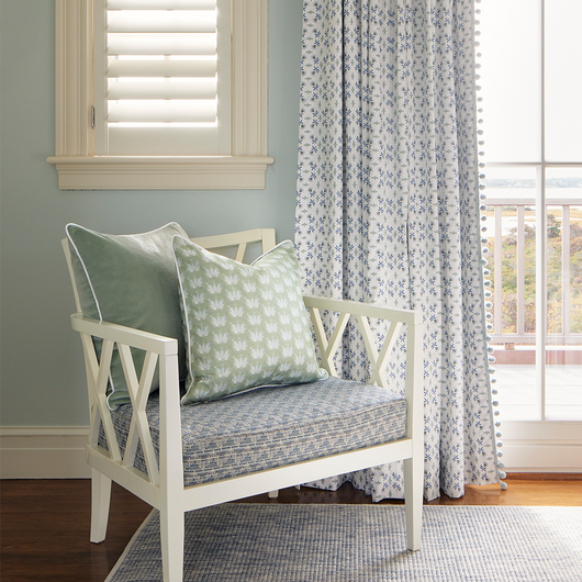 Blue & Green Floral print curtains hung in front of an illuminated window with a white chair in front of the window with blue green velvet pillow with a Blue & Green Floral Drop Repeat pattern pillow