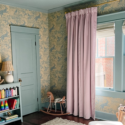 lilac velvet curtains hung on a metal rod in front of an illuminated window in a room with the trim painted blue green and yellow animal pattern wallpaper