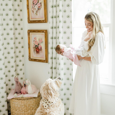 Green Floral  curtains hung in front of an illuminated window with a mom holding her baby in front of the window and a framed picture of a bouquet of flowers on the wall