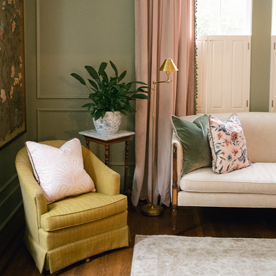 pink velvet curtains hung in front of a window with sage green tassels, fern green velvet pillow and a Rose pink Chinoiserie pillow on a white couch, a yellow chair with pink palm print pillow on the chair