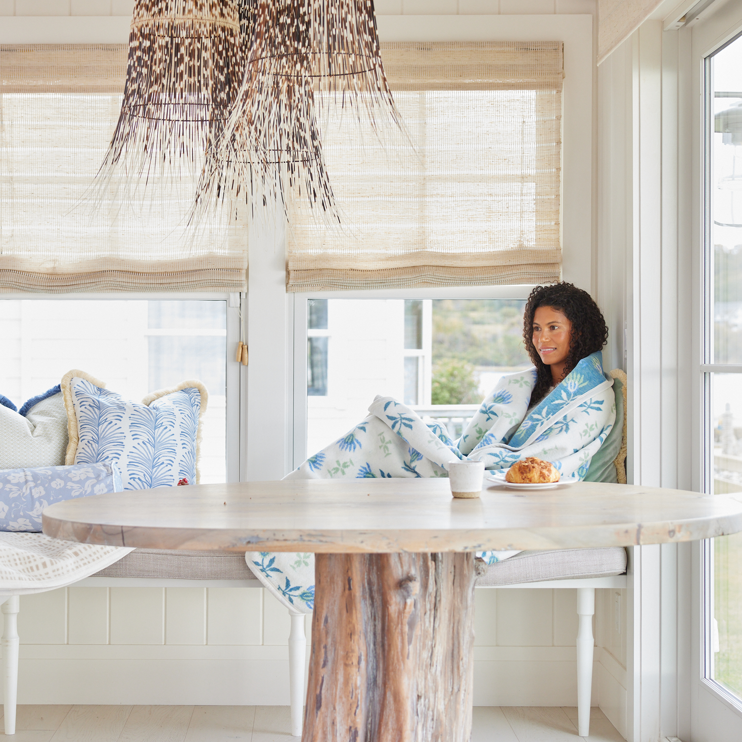 Breakfast bench with a woman next to a Sky Blue Botanical Stripe Pillow and a Blue and Green Floral Blanket.