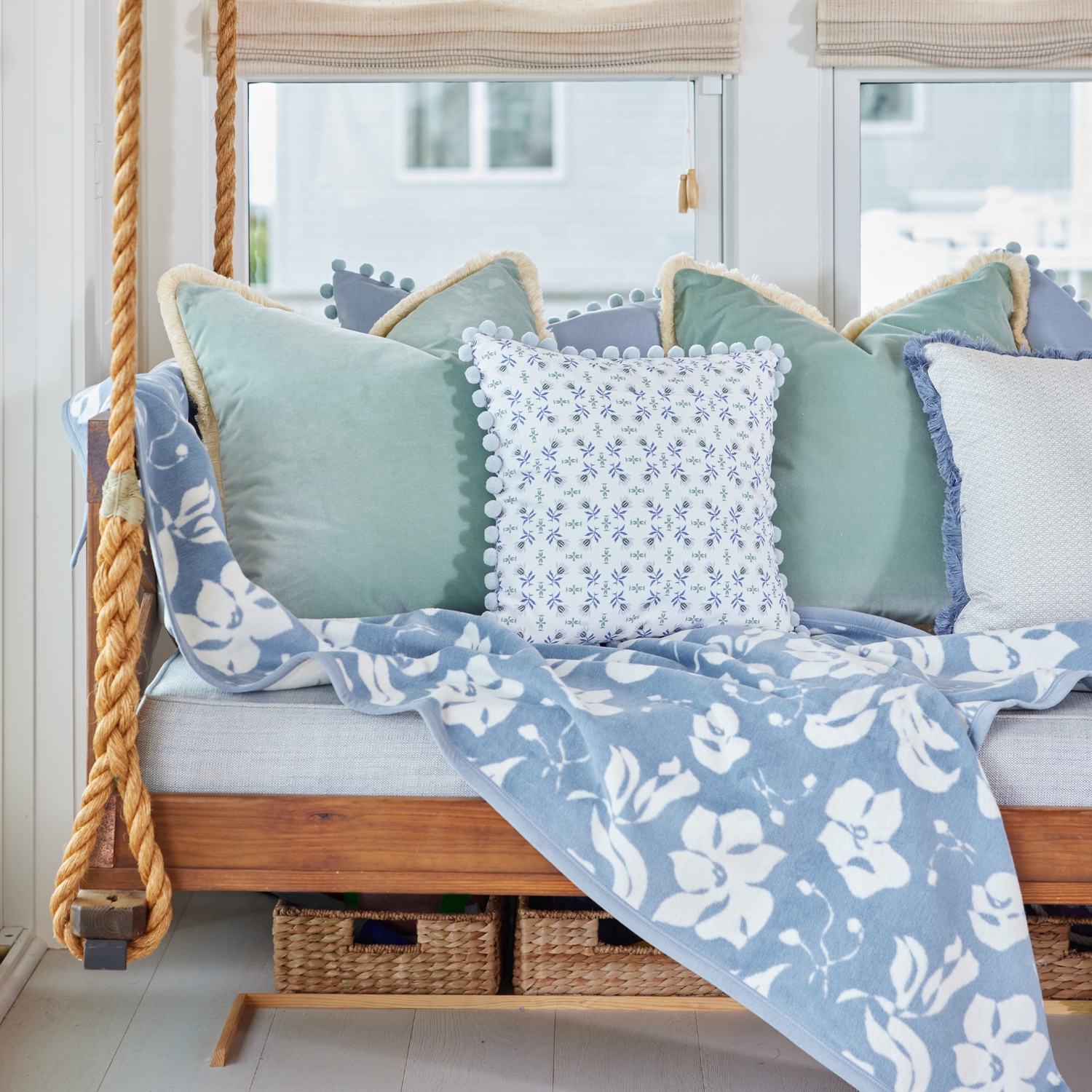 Bench with Mint Green and Sky Velvet Pillows, a Geometric Floral Pillow with Blue Pom Poms, and a Blue Floral Blanket.