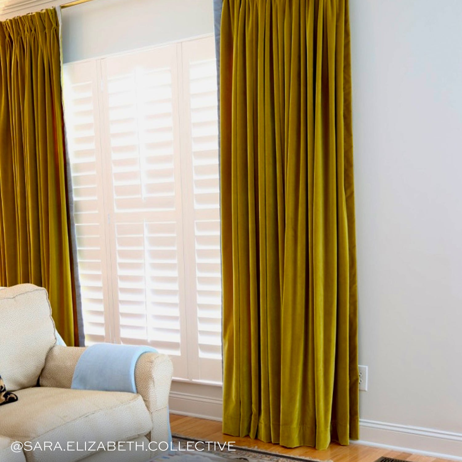 Golden chartreuse velvet curtains hung in front of an illuminated window with a white couch in front of them 