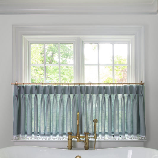 grey blue fabric curtain on a metal rod in front of an illuminated window in a bathroom