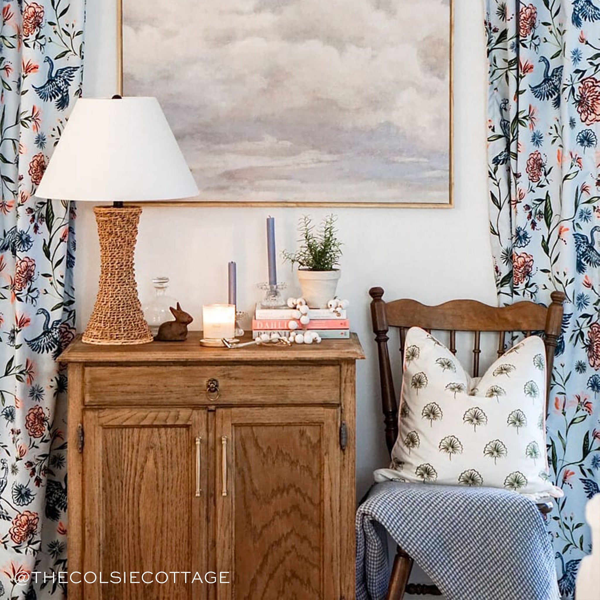 Blue Chinoiserie Printed Curtains on the sides of wooden chair with green floral pillow and navy blanket by wooden dresser with lamp, lavender candles, plant, and books stacked on top. Photo taken by The Colsie Cottage
