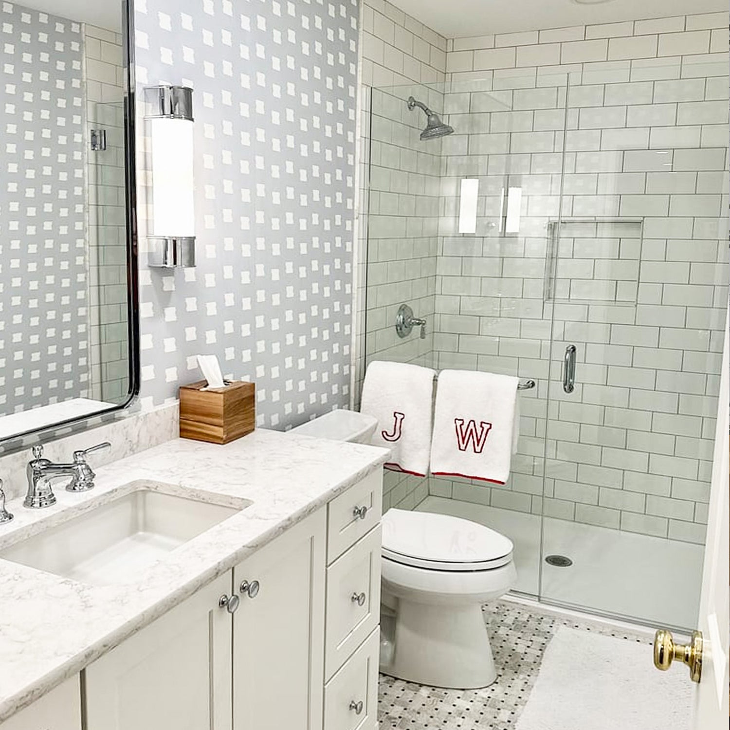 Bathroom styled with Sky Blue Pattern Printed Wallpaper next to a white granite sink and clear shower with two monogrammed towels hanging by white toilet