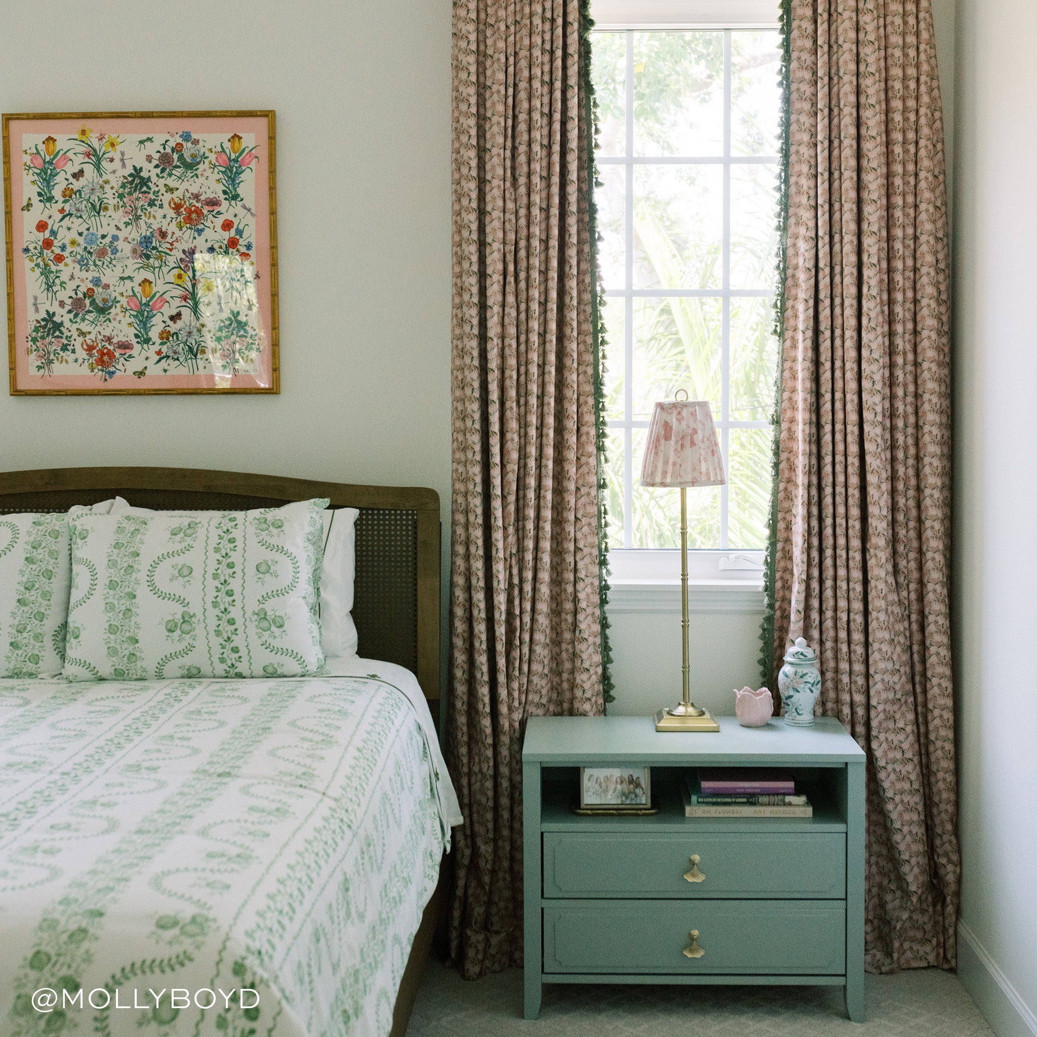 Bedroom styled with pink and gold lamp on turquoise night stand in front of window with Pink Floral Printed Curtains with Sage Tassel next to white bed with green designs under floral artwork on top. Photo taken by Molly Boyd