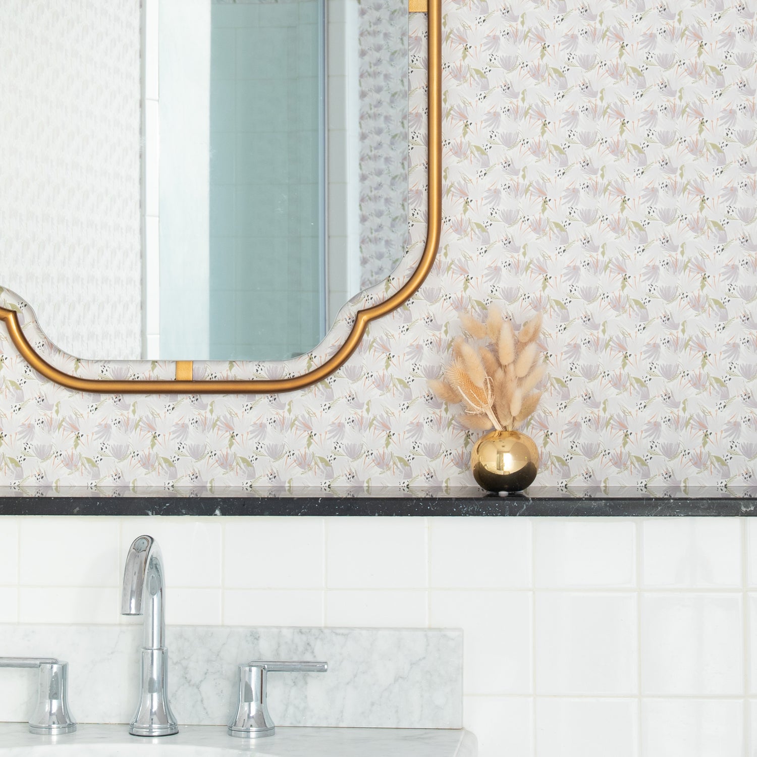 Bathroom styled with gold mirror on Grey Floral Printed Wallpaper with decorations in gold vase on black marble counter on top of silver sink with grey marble