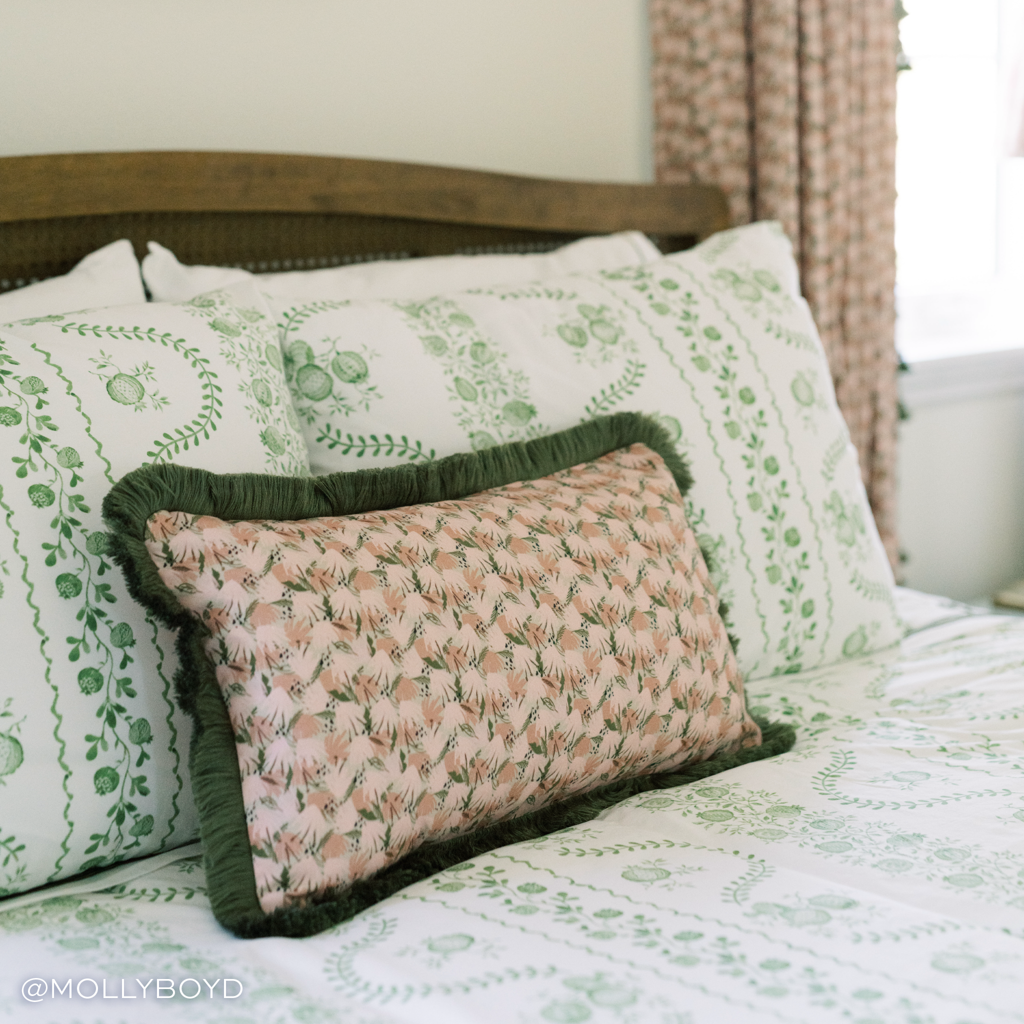 pink and green floral pillow with green fringe trim laying on green and white floral bedding