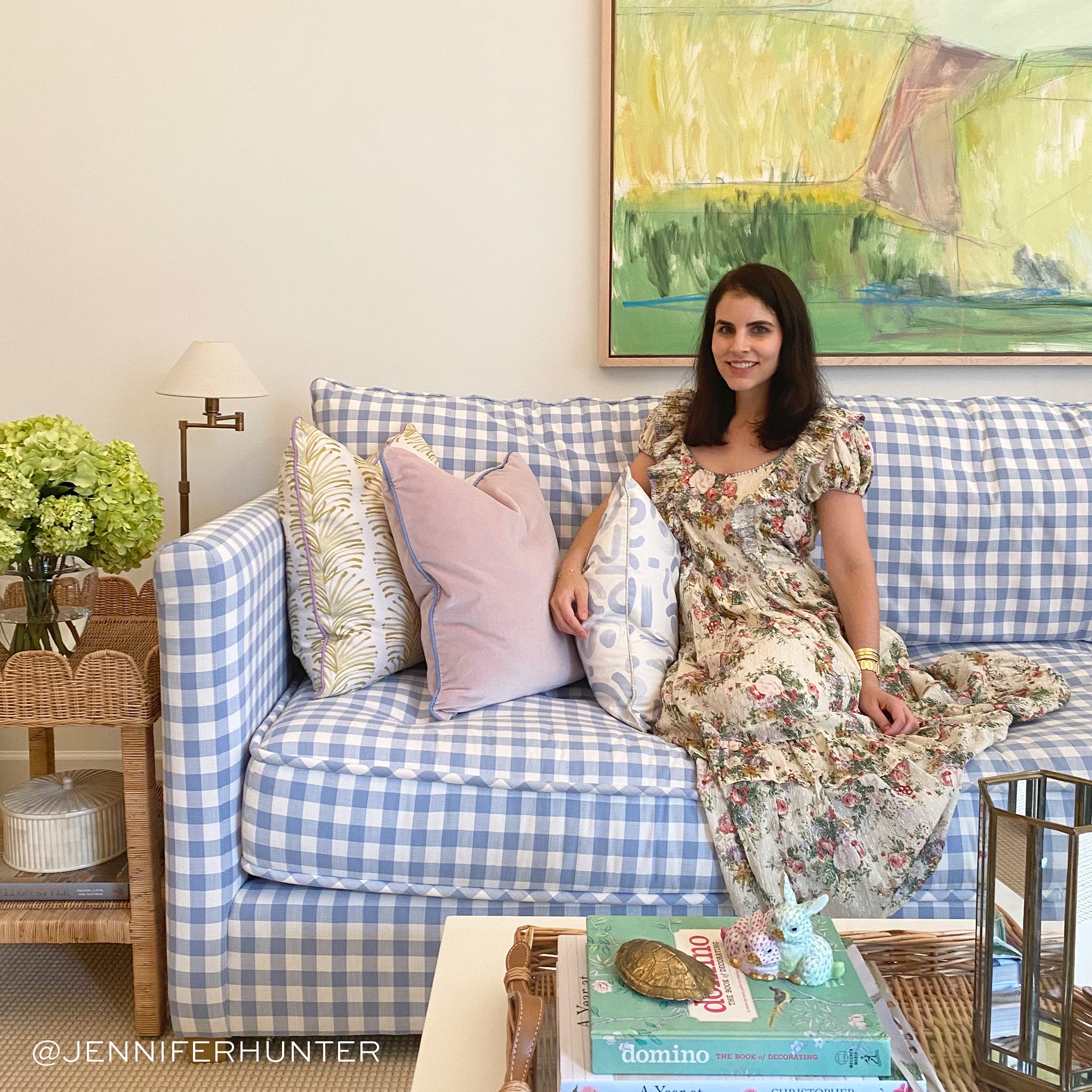 Living room styled with Yellow Stripe Chartreuse Printed pillow, pink velvet pillow, and sky blue printed pillow on blue and white couch next to brunette woman wearing a cream floral dress next to white coffee table with books and decorations. Photo taken by Jennifer Hunter