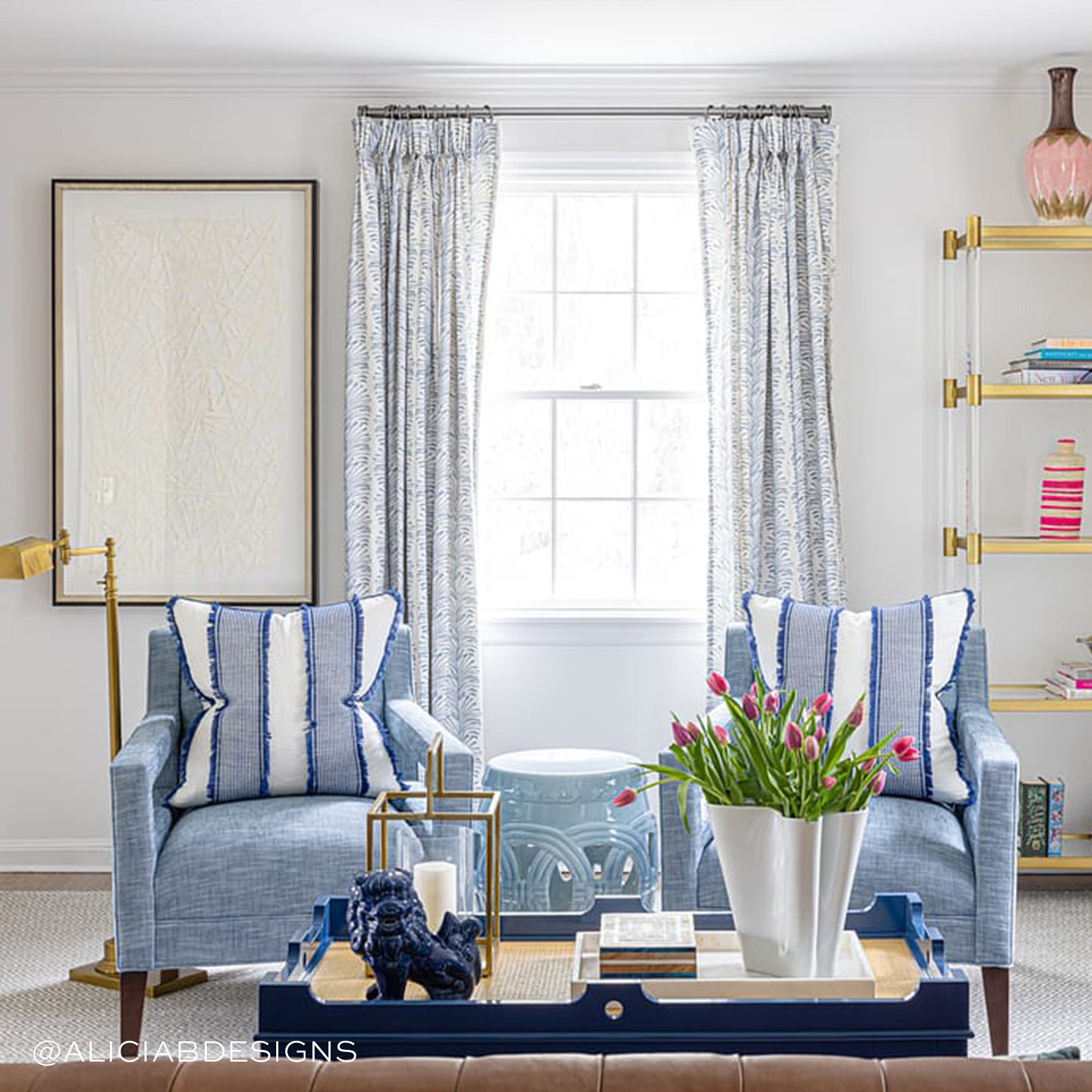 Living room styled with Sky Blue Palm Printed Curtains and two blue sofa chairs with striped blue and white pillows next to pink flowers in white vase on blue coffee table. Photo taken by Alicia B Designs
