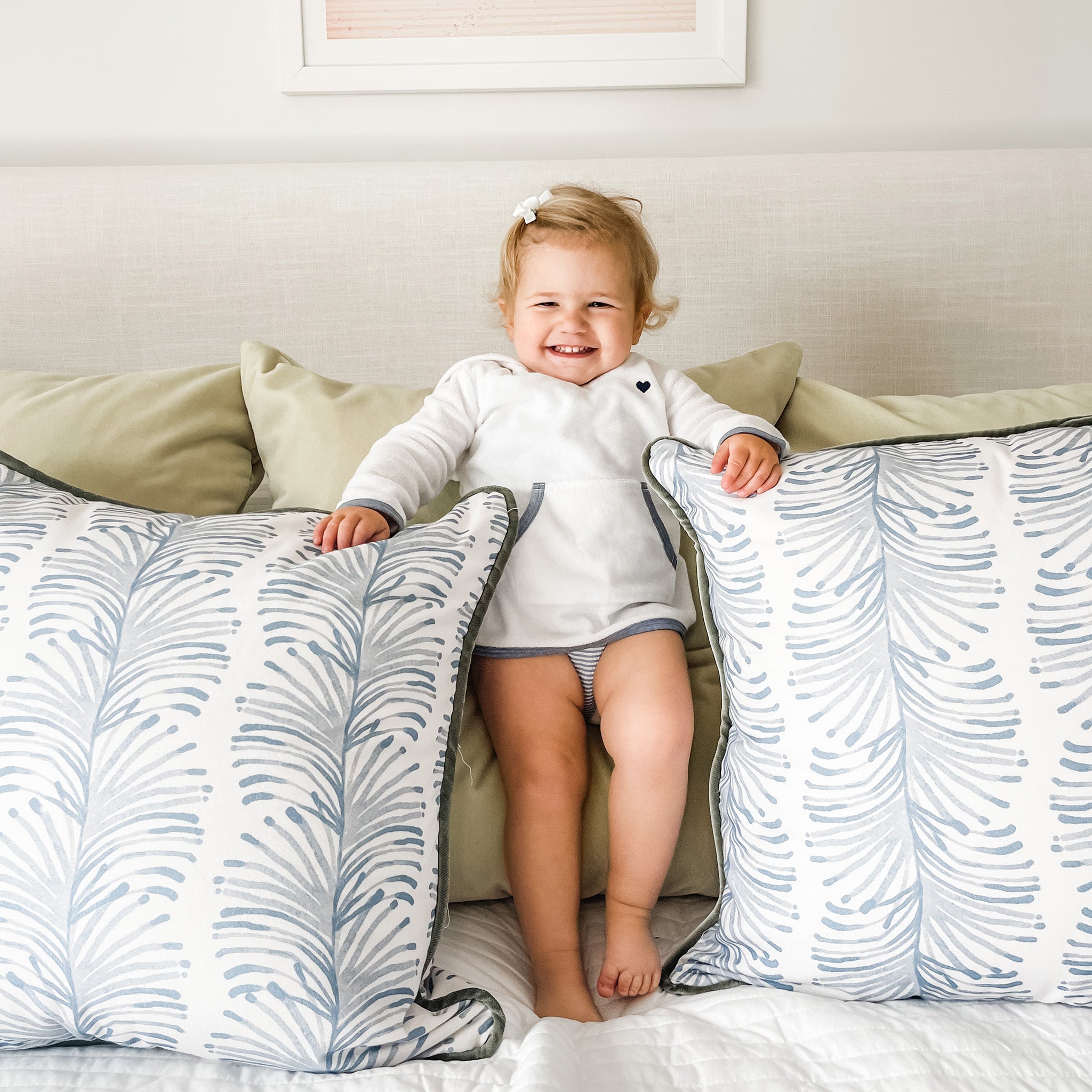 Bed Close-up with blonde joyous baby wearing white long sleeve in between two Sky Blue Botanical Stripe Printed Pillows