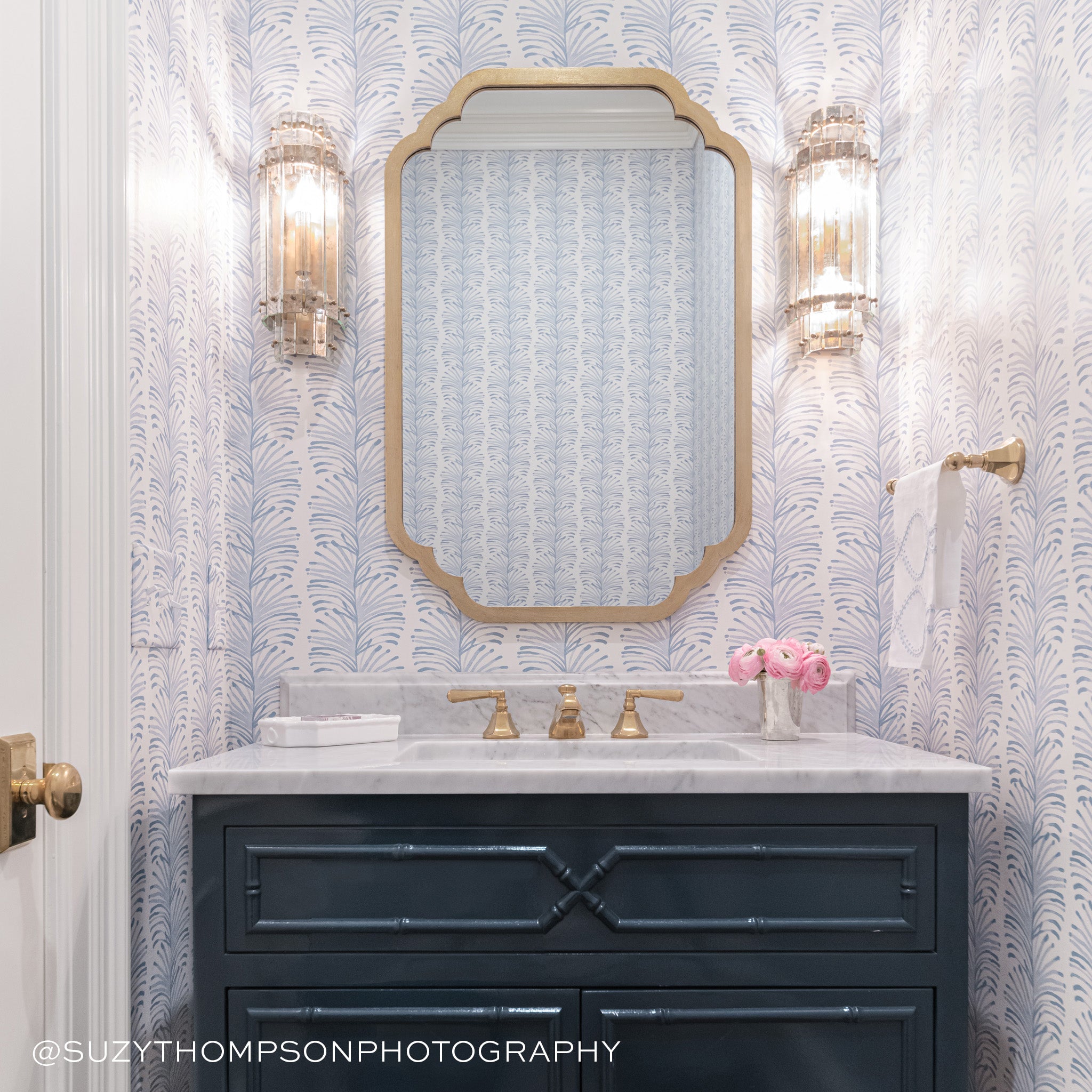 White marble bathroom sink styled with Sky Blue Botanical Stripe Printed Wallpaper with gold mirror hung in the center and two lamps by the side. Photo taken by Suzy Thompson