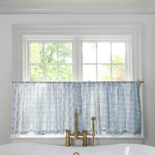 Sky Blue Botanical Stripe Printed Cotton fabric curtain on a metal rod in front of an illuminated window in a bathroom 