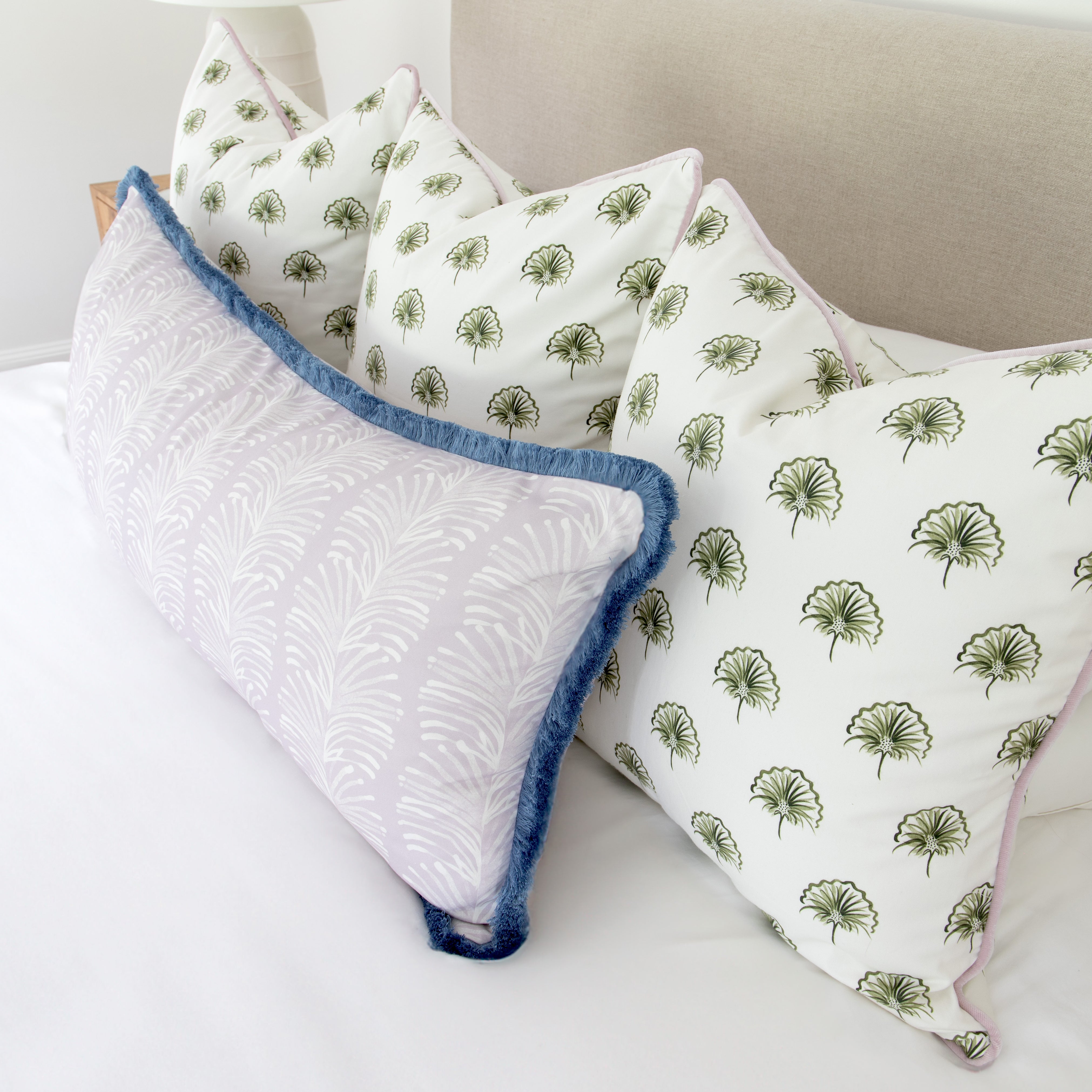 Bedroom close-up with three green floral printed pillows and one Lavender Botanical Stripe printed lumbar with blue fringe on top of white bed