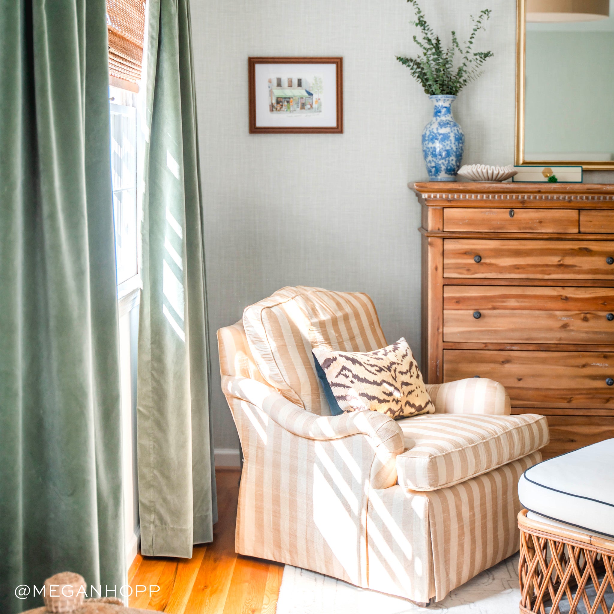 Corner styled with Fern Green Velvet Curtains next to striped couch with zebra printed pillow next to wooden dresser and plants in blue and white vase on top. Photo taken by Megan Hopp