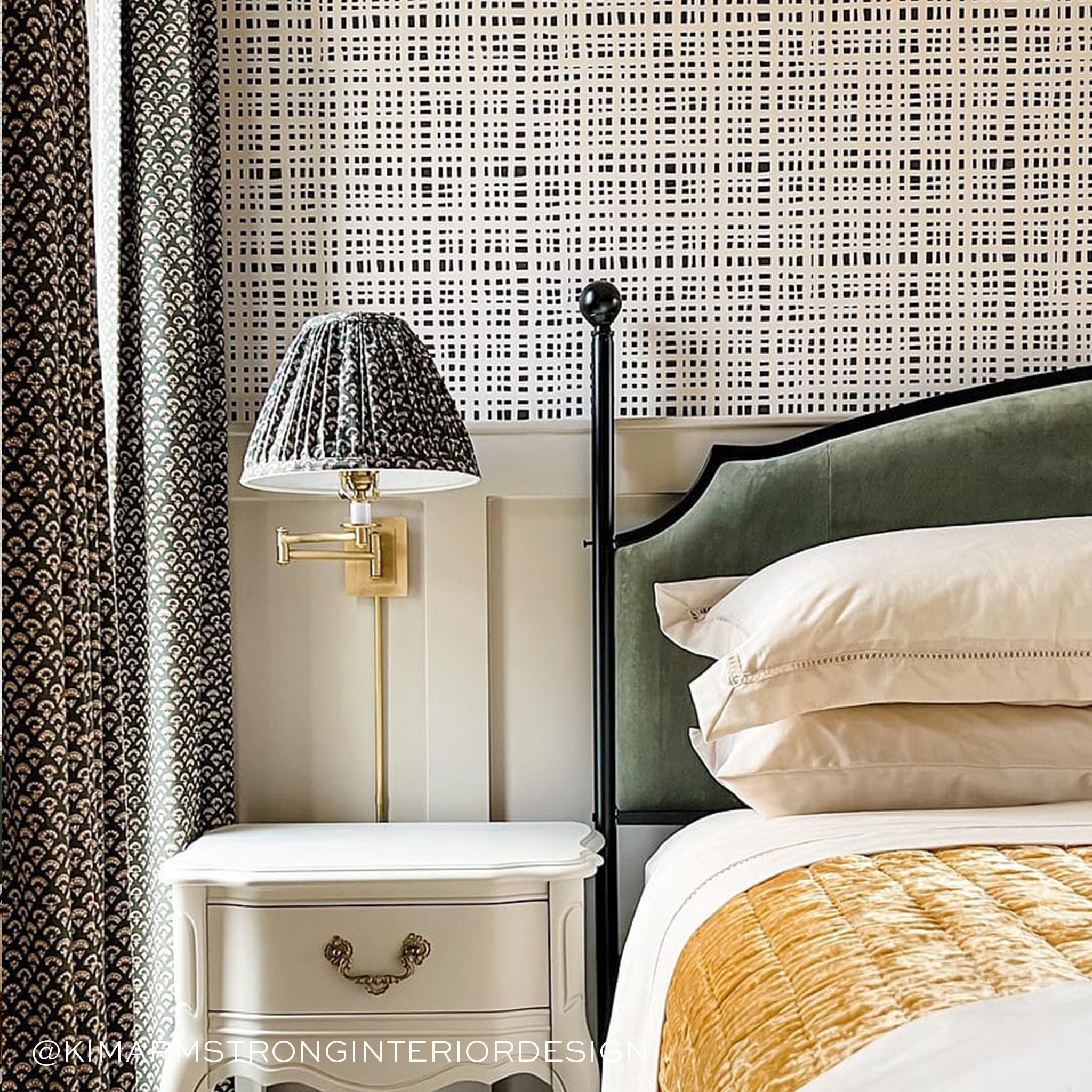 Close-up of white nightstand with black and white lamp and white and black and white curtains next to bed styled with a fern green velvet bed frame and cream sheets and pillows. Photo taken by Kim Armstrong