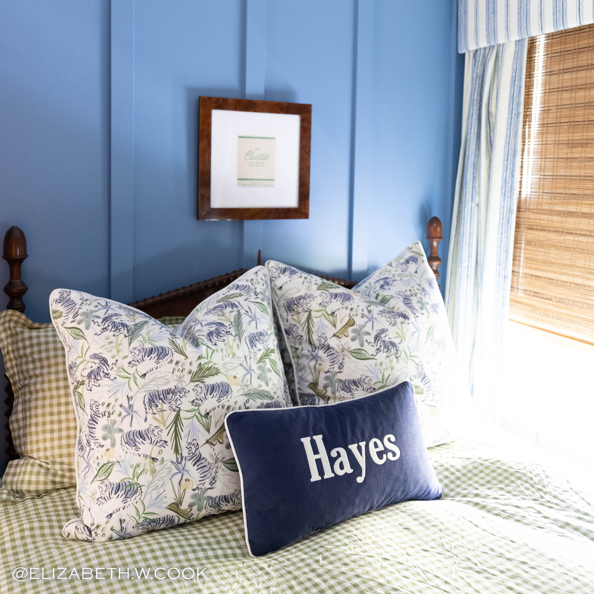 Bedroom styled with floral green and blue pillows and a navy blue pillow with sky blue piping and embroidery saying "Hayes" on a green checkered bed in front of window