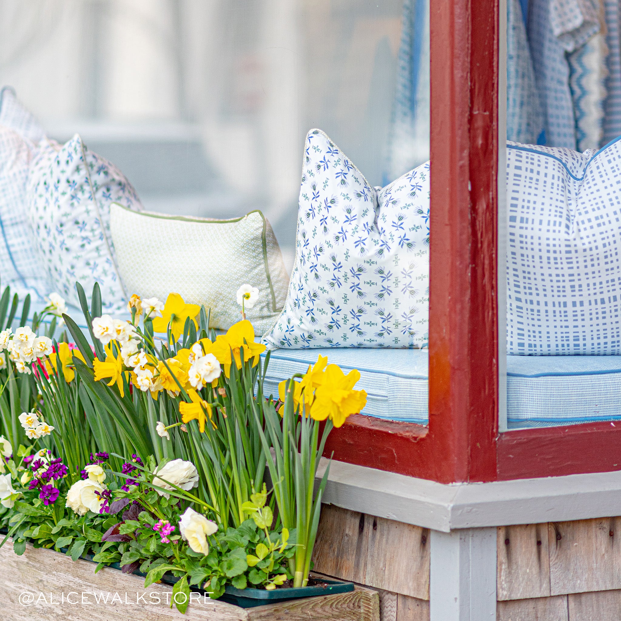 Window Store Close-Up styled with flowers on front and blue mattress inside with Sky Blue Gingham Printed Pillow, Blue & Green Striped Printed Pillow, and Moss Green Geometric Printed Lumbar in the center. Photo taken by Alice Walk Store