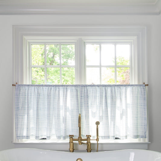 Sky Blue Gingham Printed Cotton fabric curtain on a metal rod in front of an illuminated window in a bathroom