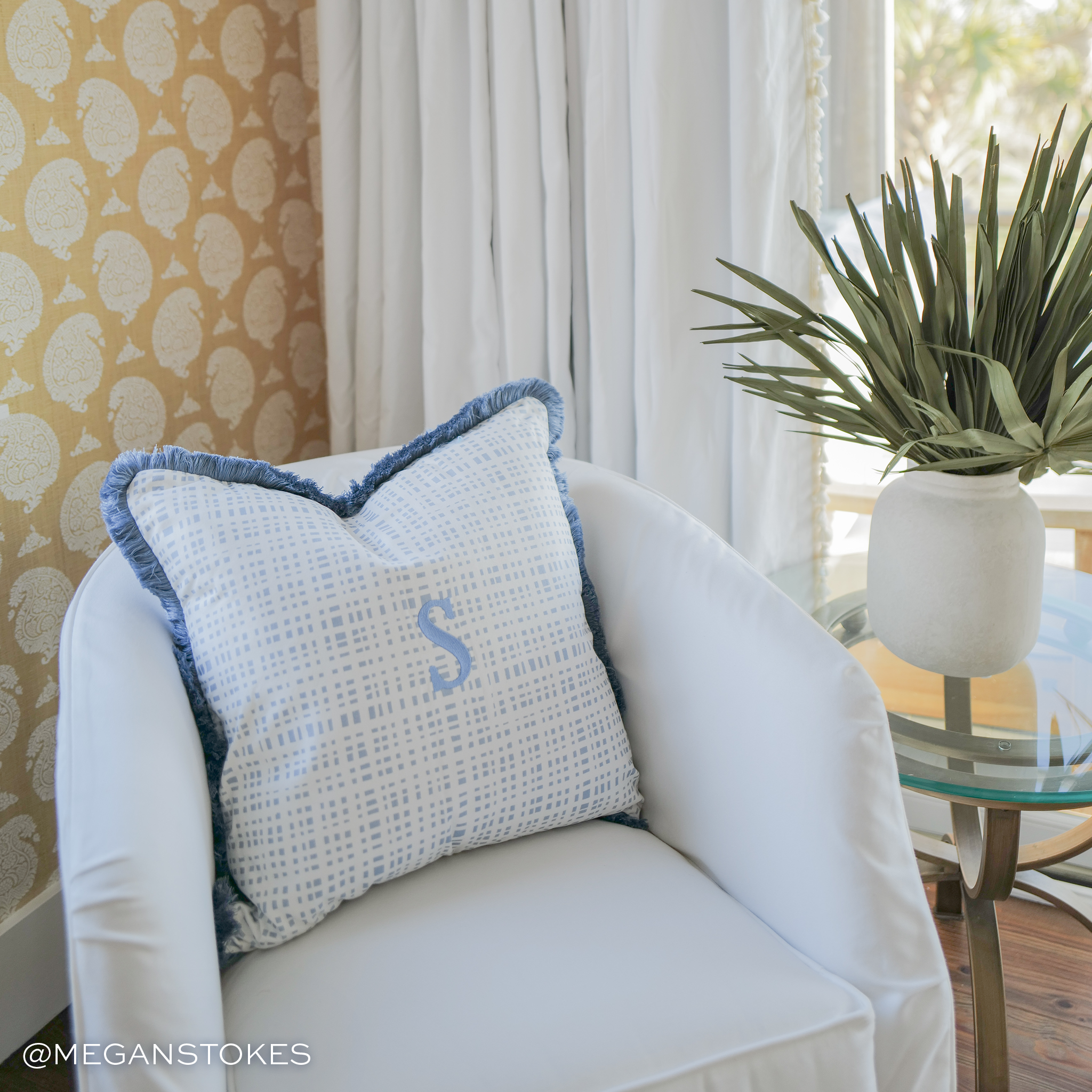 white chair in a yellow wallpapered room with a light blue and white plaid pillow with an embroidered light blue "S"