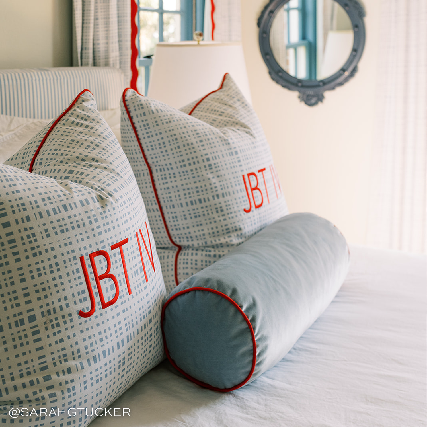 light blue plaid pillows with red trim and a solid light blue velvet pillow in front with red trim on a white bed