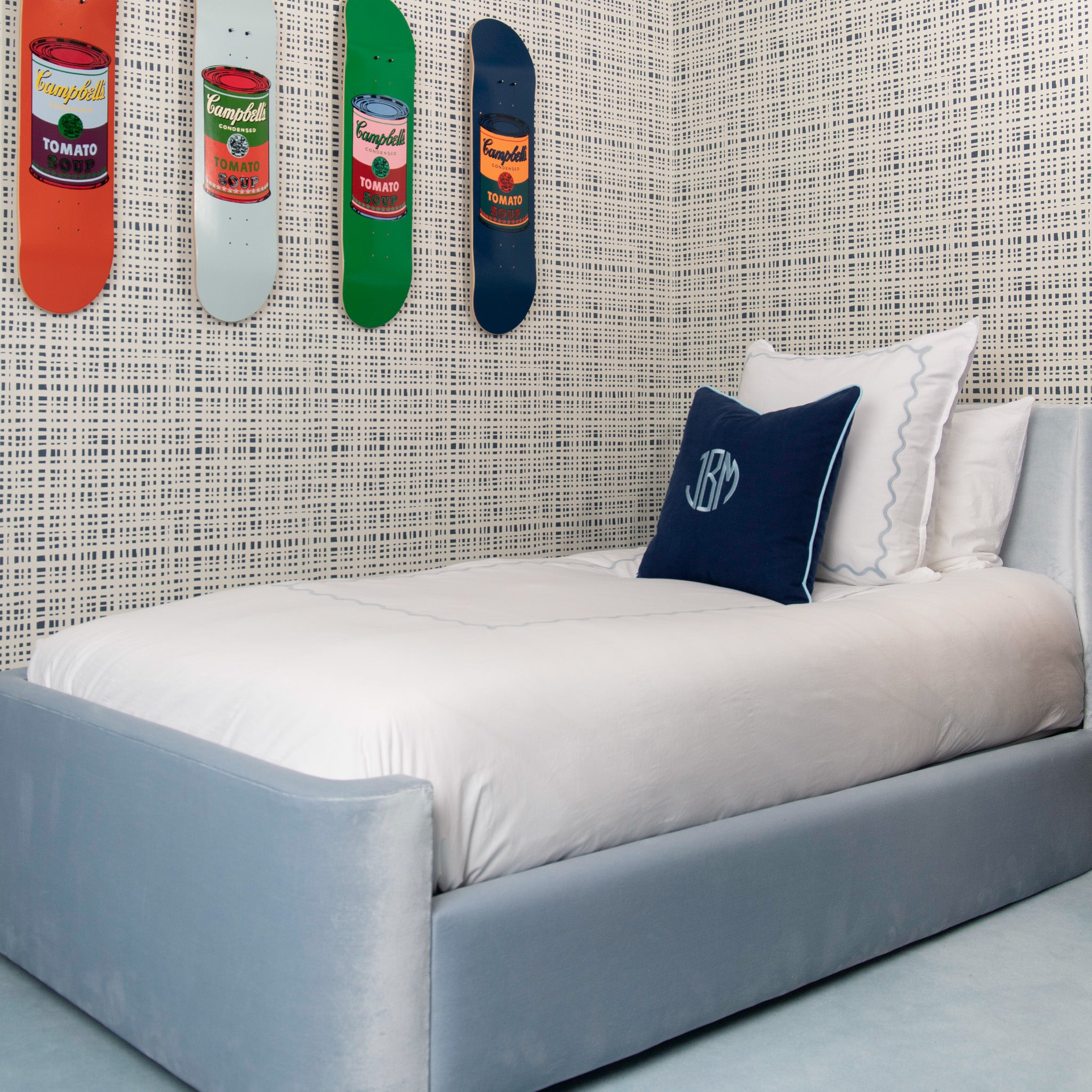 Boys bedroom styled with navy gingham printed wallpaper with four hanging skate boards by white bed with navy blue monogrammed pillow 
