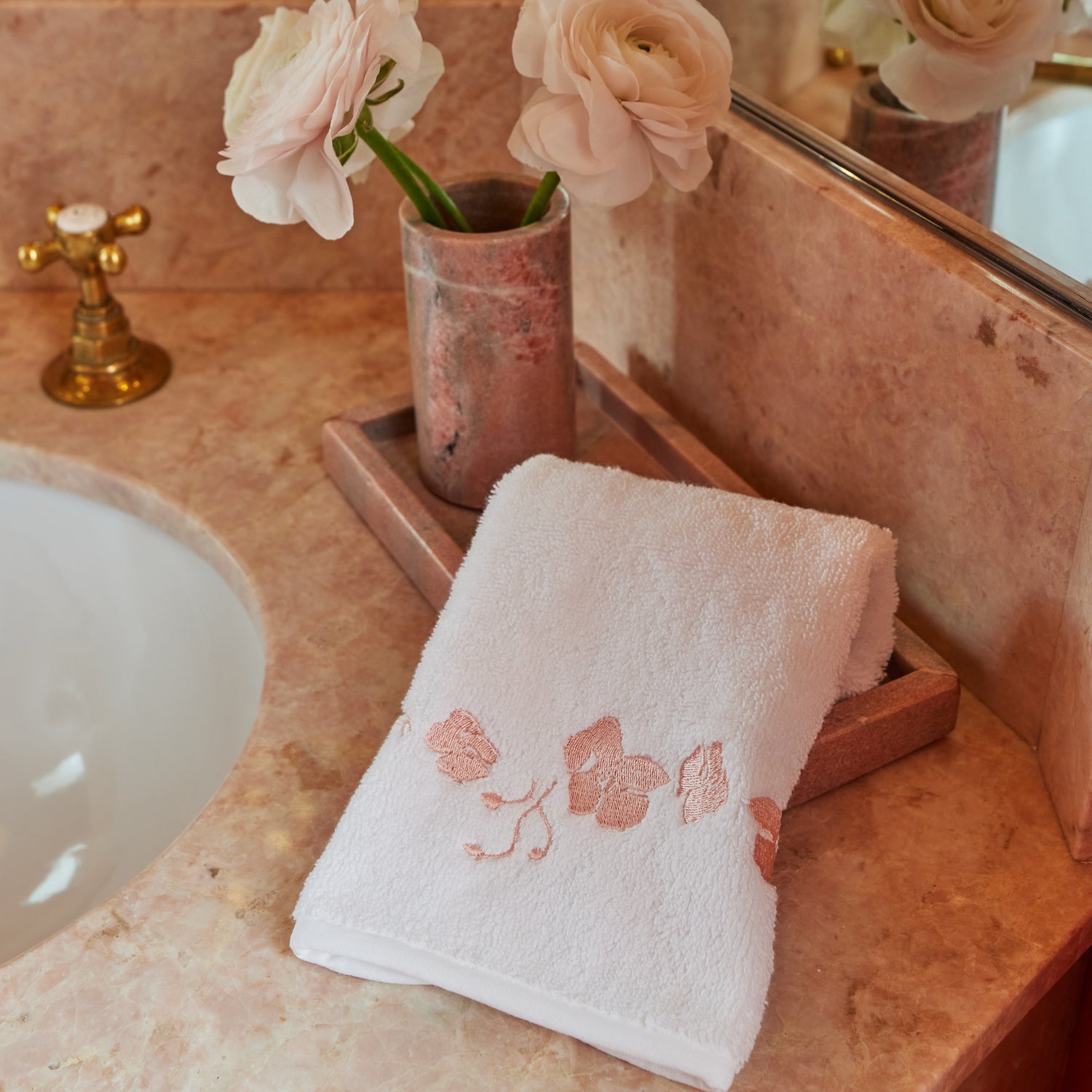 white towel with coral embroidered botanical stripe pattern on a pink marble bathroom counter