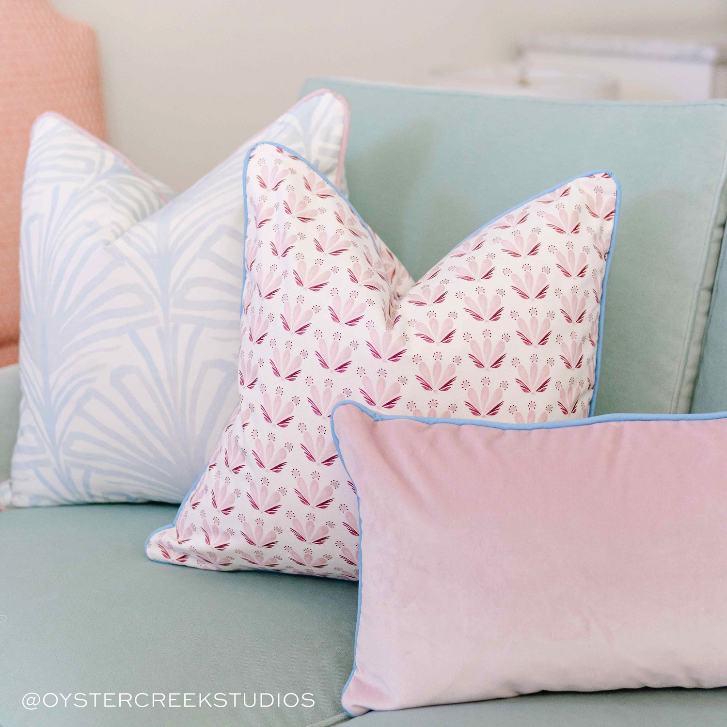 Close-up of Sky Blue Palm Printed Pillow, Pink & Burgundy Drop Repeat Floral Printed Pillow, and Pink Velvet Lumbar on a Blue Green Couch. Photo taken by Oyster Creek Studios
