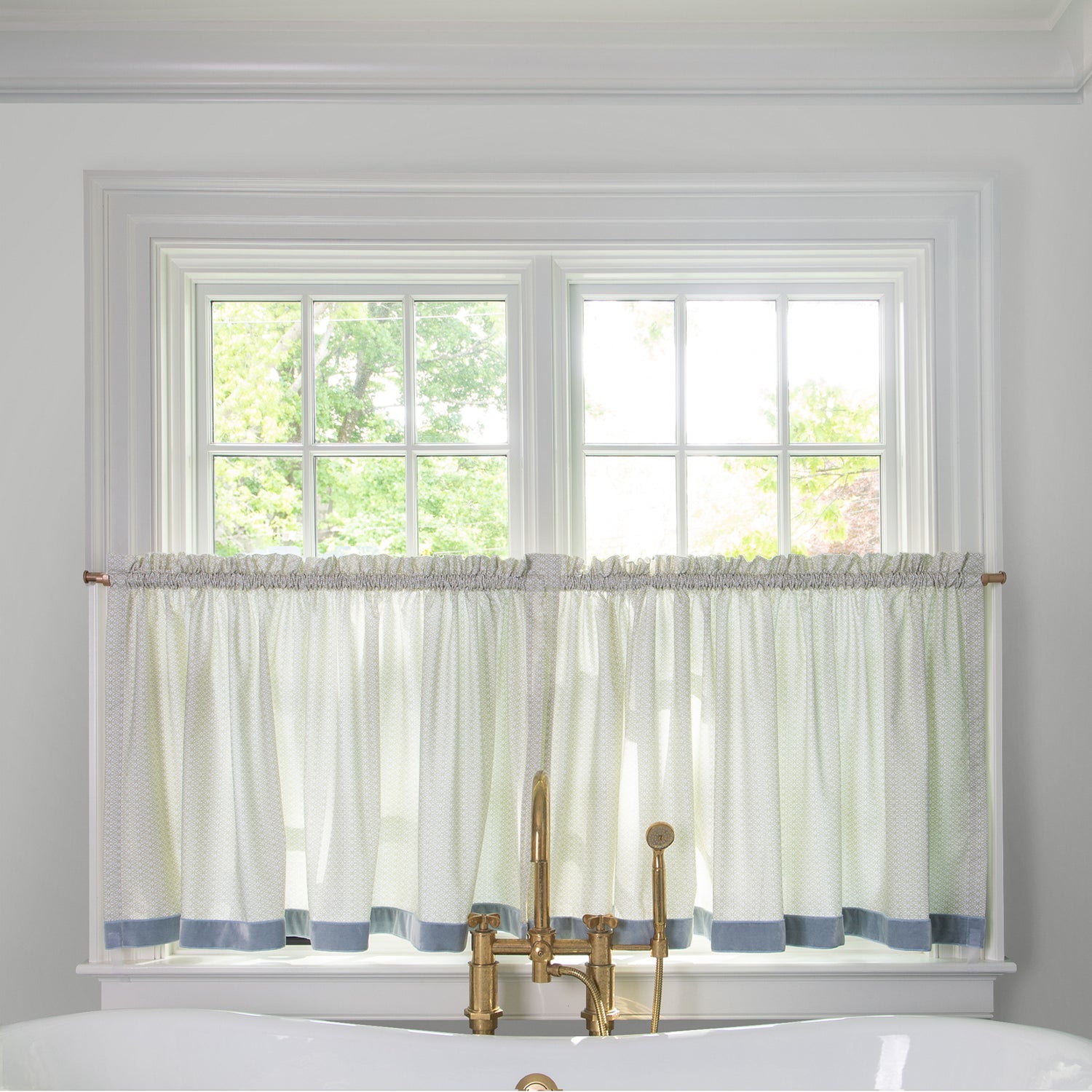 Moss Green Geometric Printed curtain on a metal rod in front of an illuminated window in a bathroom