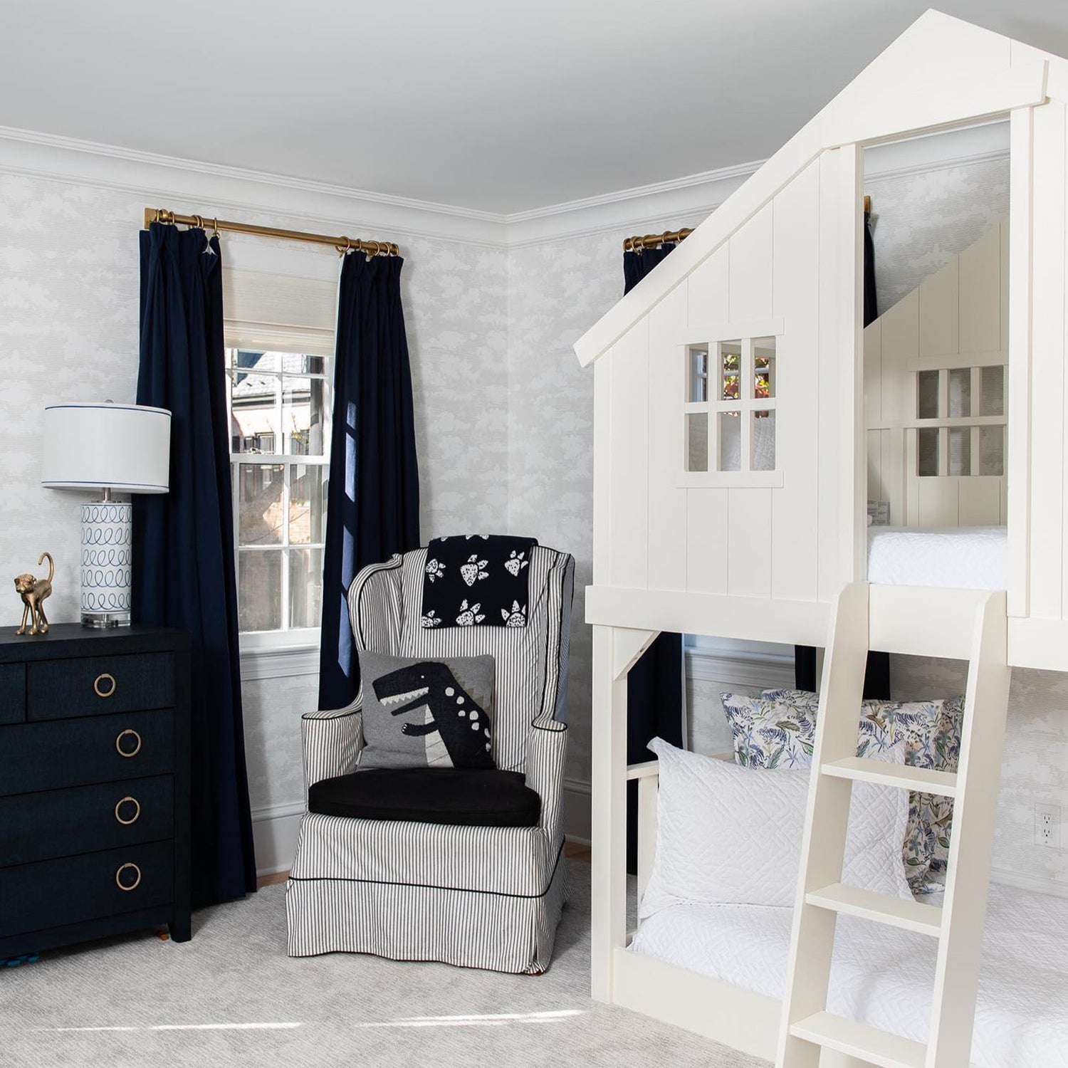 Children's bedroom styled with Navy Blue Curtains on two windows in front of white house bed with Blue With Intricate Tiger Design Printed pillows by striped sofa chair with dinosaur printed pillow and navy blue dresser next to it