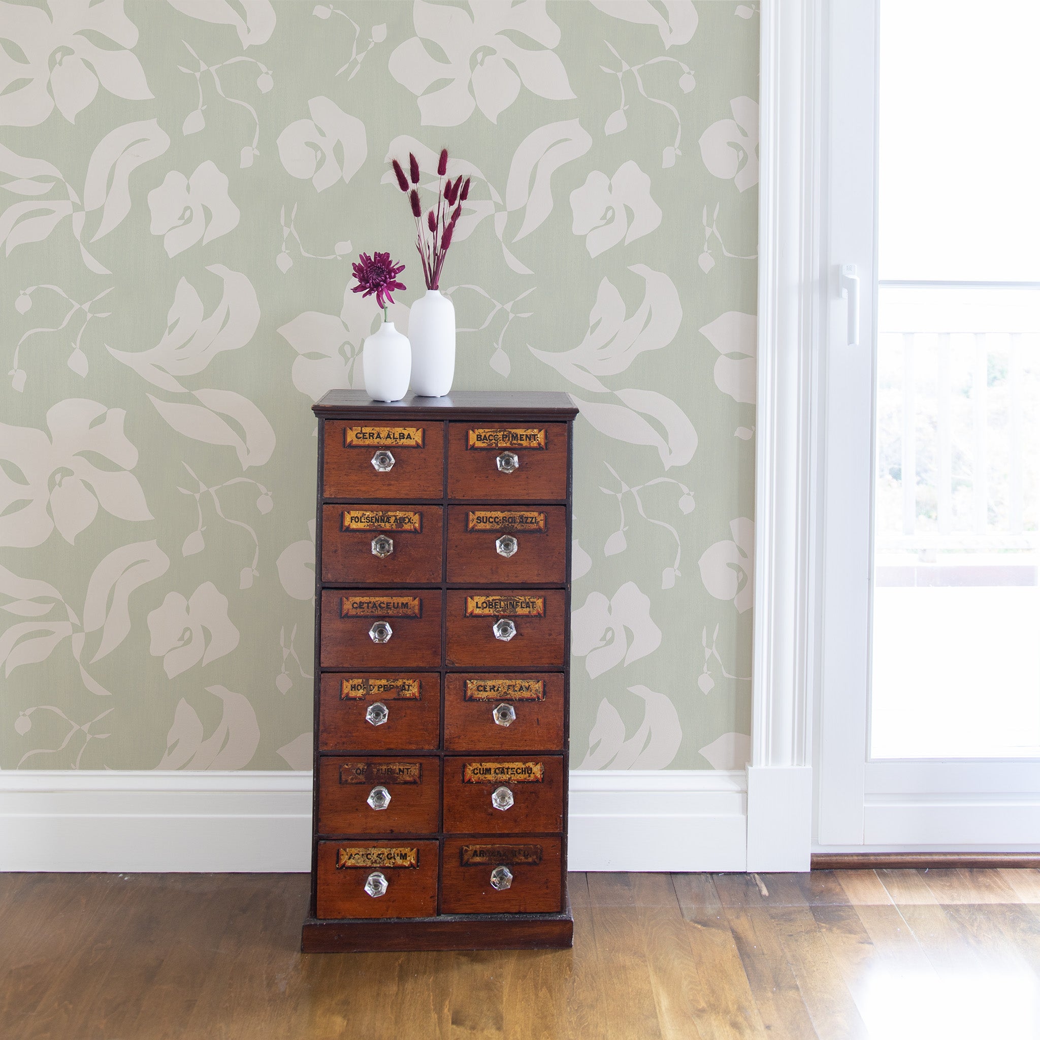 wall with green and white floral wallpaper and a brown cabinet with white vases and red flowers