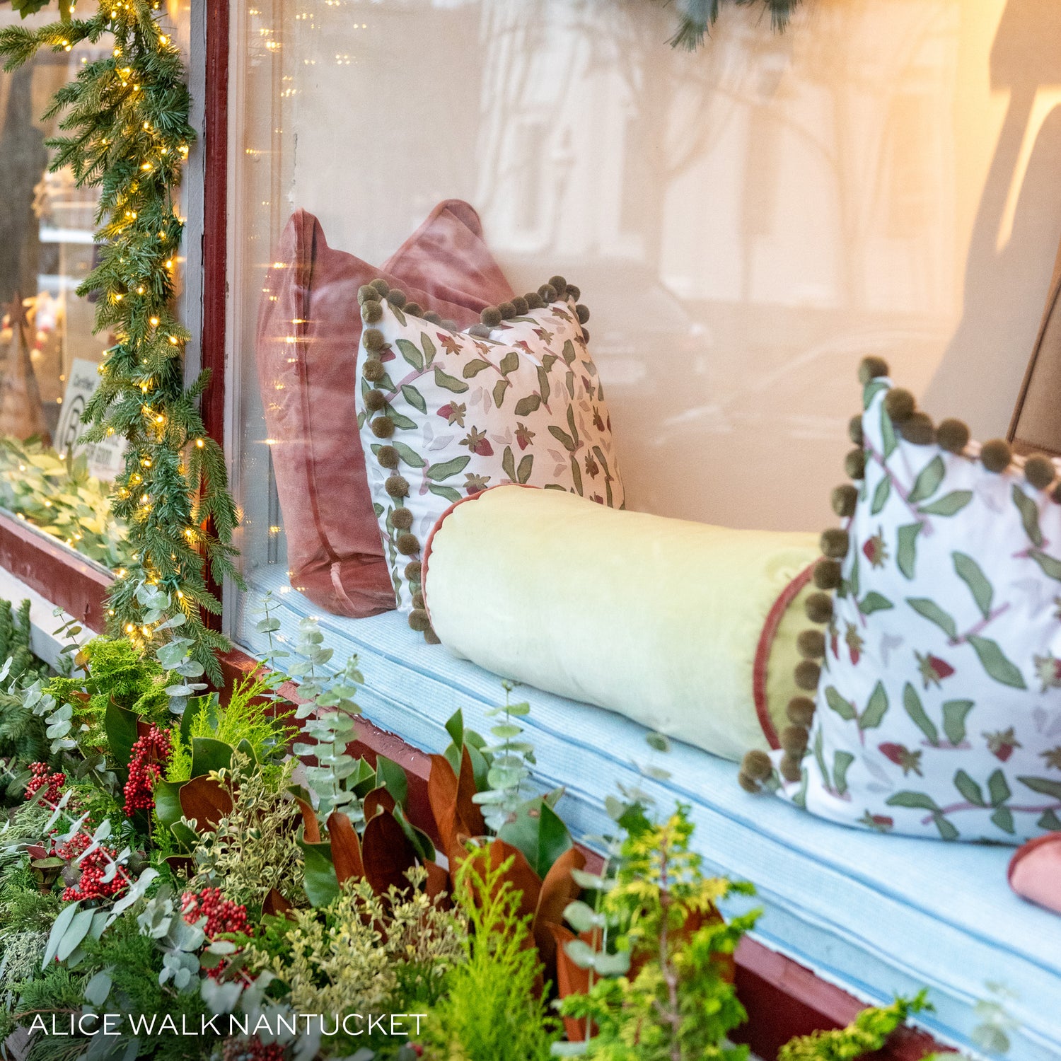 exterior image of a window with four green and dark pink pillows on a blue window bench