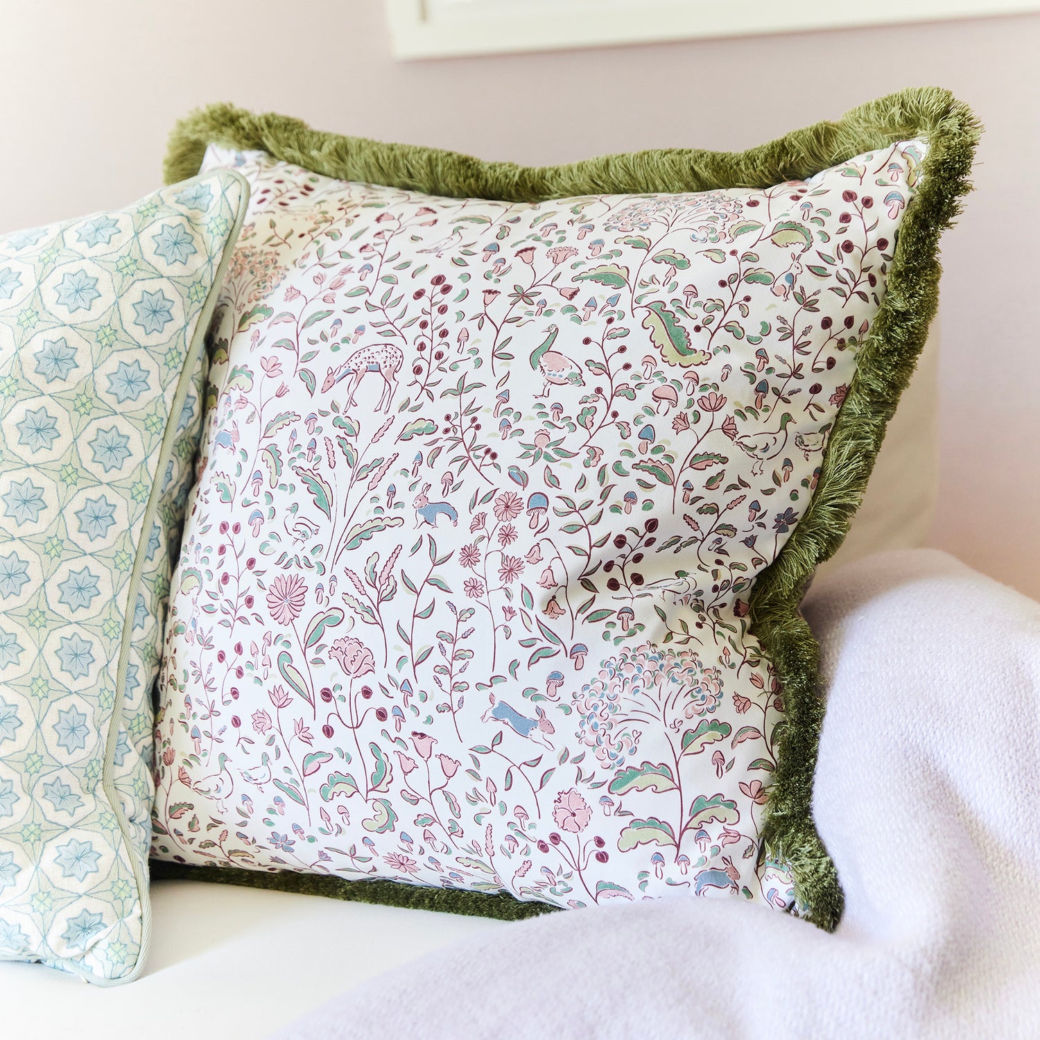 Decorative floral and nature print pillow with green fringe trim on a white couch by BY Interiors