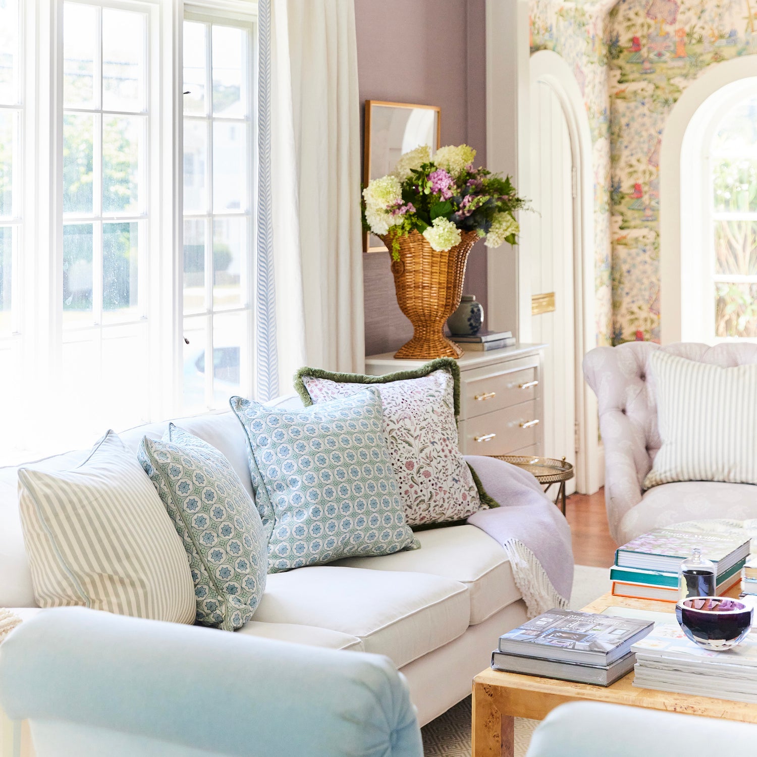 Bright living room with BY Interiors pillows in soft patterns, fresh floral arrangement, and cozy light-filled seating area