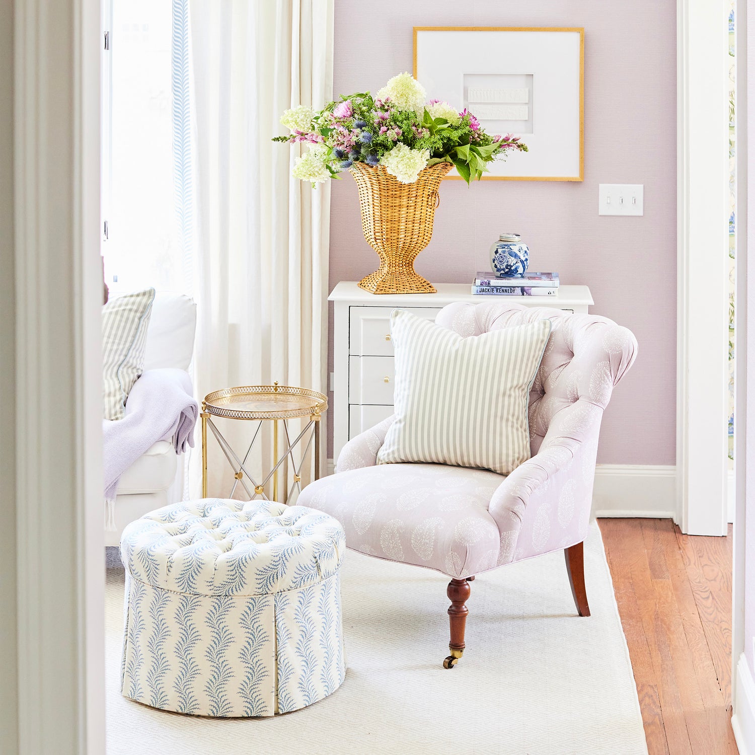 Louisa Sage light pink tufted chair with striped pillow beside patterned ottoman in bright cozy room with floral arrangement