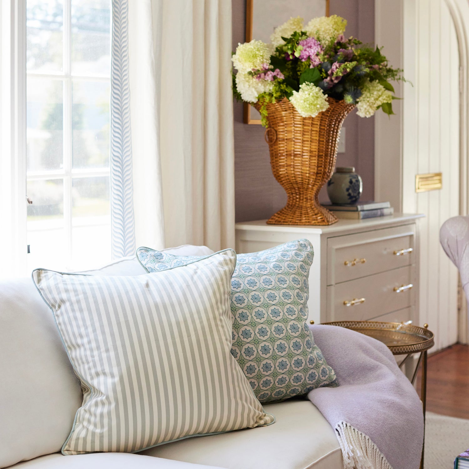 Cozy living room with striped and patterned pillows on a sofa alongside a lavender throw by BY Interiors